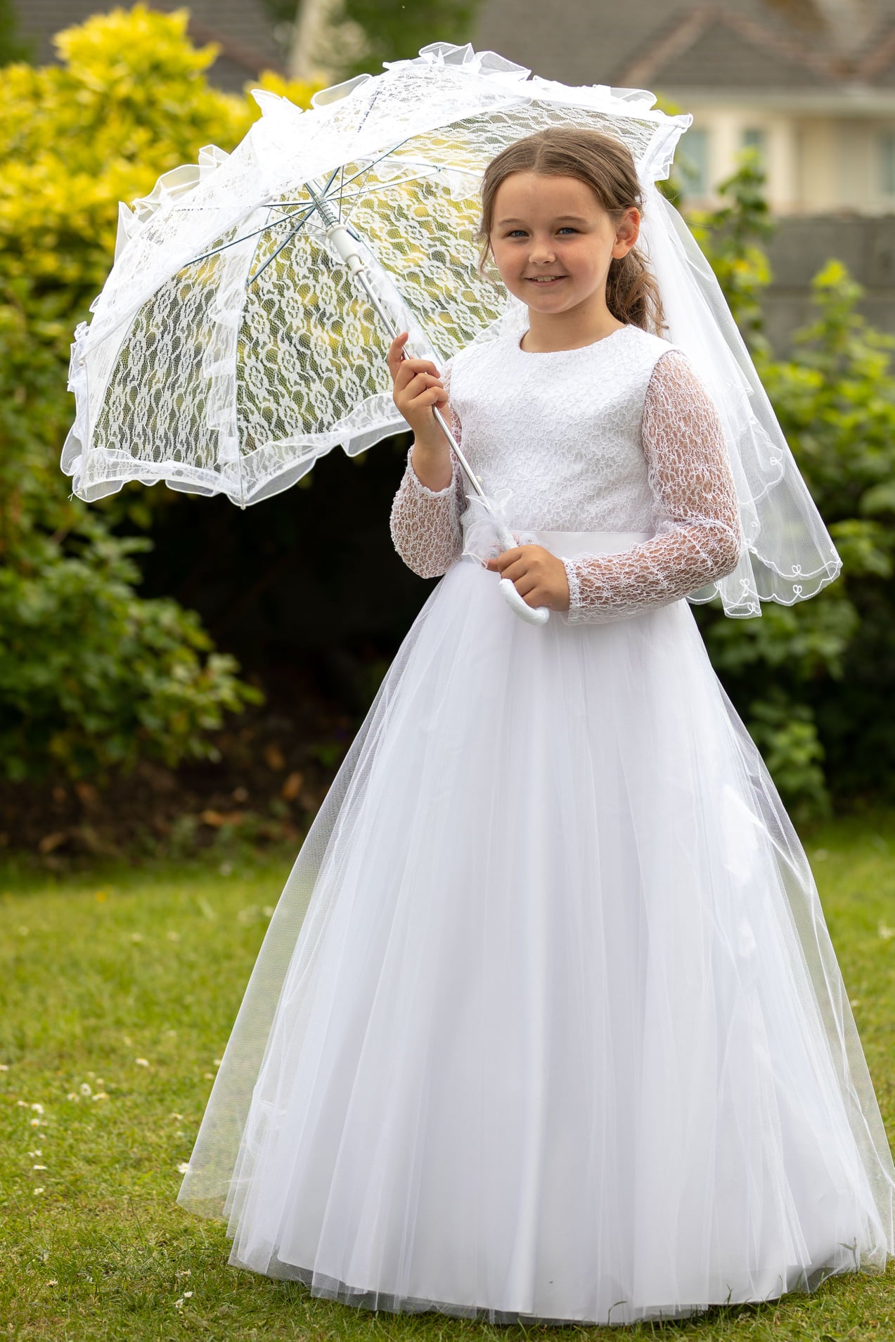A girl wearing a brand-new white lace communion dress with a veil and parasol